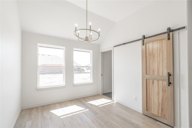 interior space with a barn door, light wood finished floors, baseboards, a chandelier, and vaulted ceiling