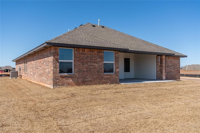 rear view of property featuring a patio, cooling unit, brick siding, and roof with shingles