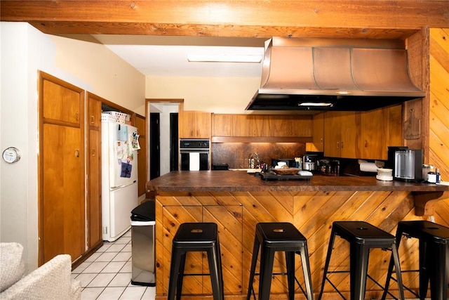 kitchen with dark countertops, wall chimney range hood, black oven, and freestanding refrigerator