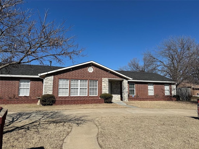 single story home with stone siding, brick siding, roof with shingles, and concrete driveway