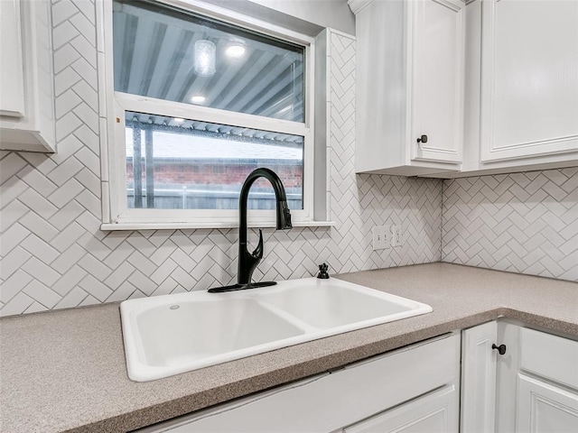 kitchen with tasteful backsplash, white cabinetry, light countertops, and a sink