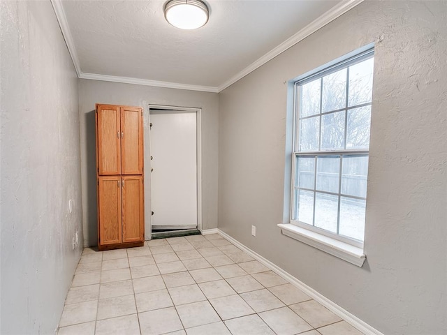 empty room featuring light tile patterned flooring, baseboards, ornamental molding, and a textured wall