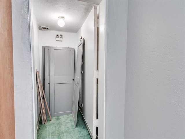 corridor with a textured wall, visible vents, and light colored carpet