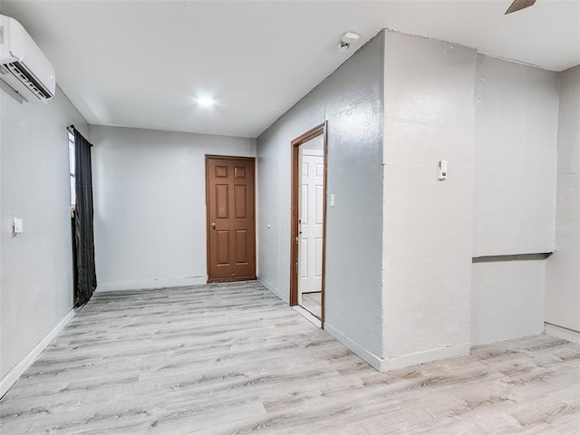 hall featuring a wall mounted air conditioner, light wood-style flooring, and baseboards