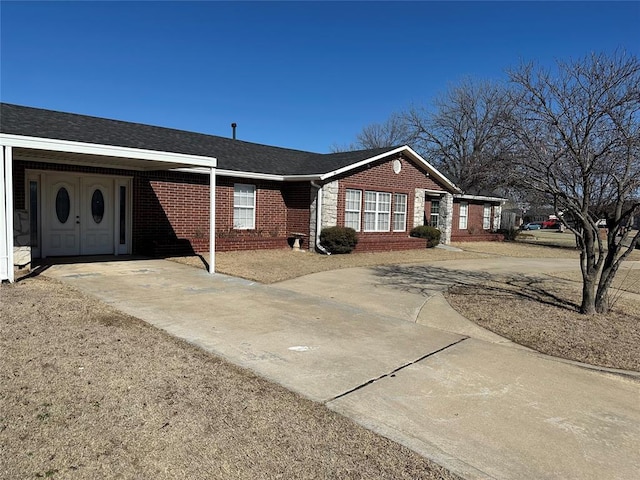 ranch-style home with a shingled roof, concrete driveway, and brick siding