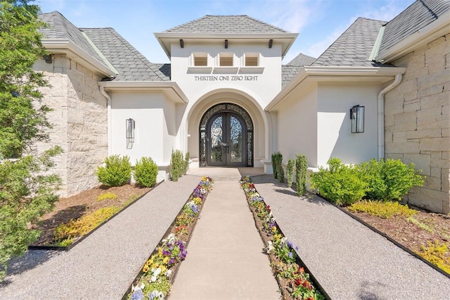 view of exterior entry featuring a shingled roof, french doors, and stucco siding