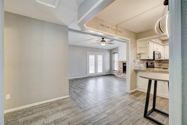 kitchen with stainless steel appliances, decorative backsplash, wood tiled floor, a brick fireplace, and white cabinets