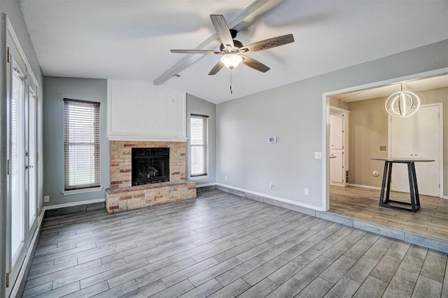 unfurnished living room featuring baseboards, a ceiling fan, lofted ceiling with beams, wood finished floors, and a brick fireplace