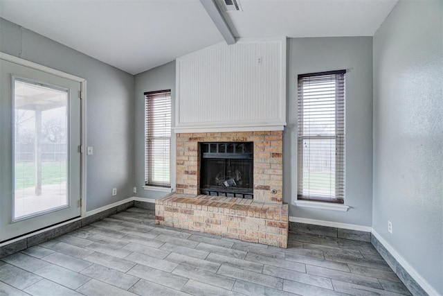 unfurnished living room with wood finish floors, a brick fireplace, lofted ceiling with beams, and baseboards