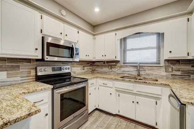 kitchen with light wood-style flooring, stainless steel appliances, a sink, decorative backsplash, and light stone countertops