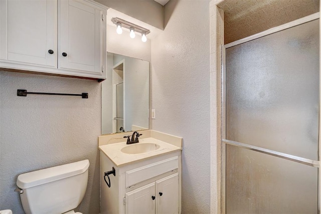 full bathroom with toilet, a stall shower, a textured wall, and vanity