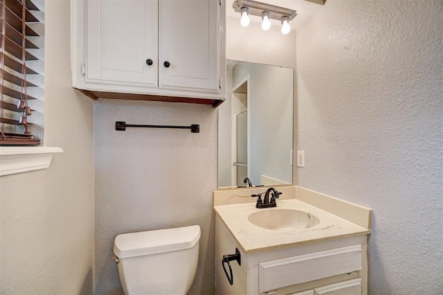 bathroom with toilet, vanity, and a textured wall