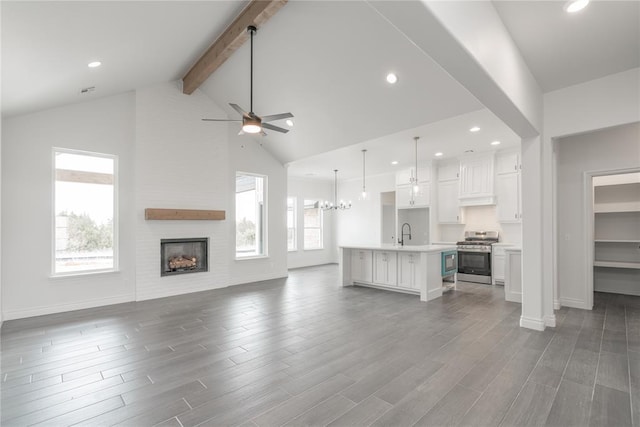 unfurnished living room featuring dark wood-style flooring, a large fireplace, beamed ceiling, and ceiling fan with notable chandelier