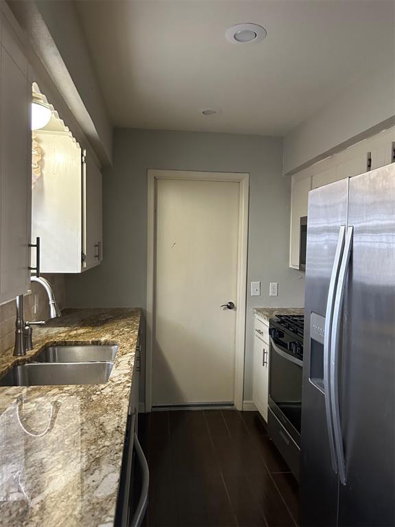 kitchen with light stone counters, a sink, white cabinetry, range with gas stovetop, and stainless steel fridge