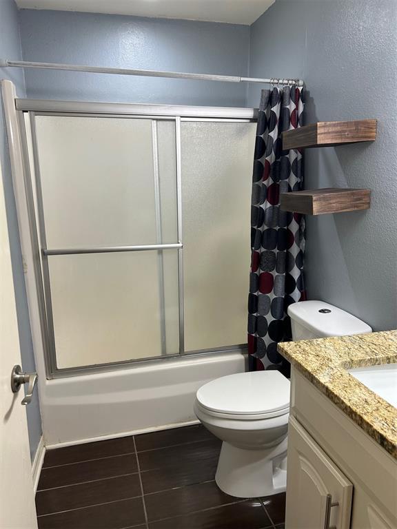 bathroom featuring wood finish floors, bath / shower combo with glass door, a textured wall, toilet, and vanity