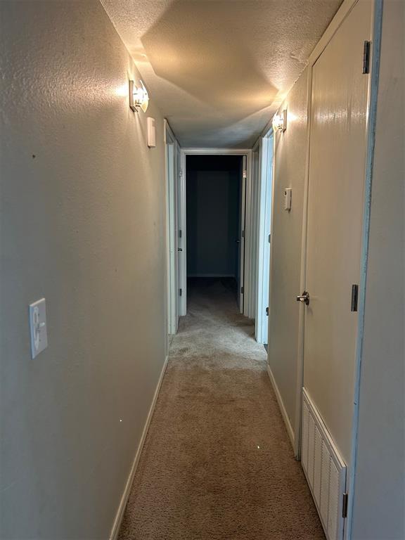 hall featuring baseboards, visible vents, light carpet, and a textured ceiling