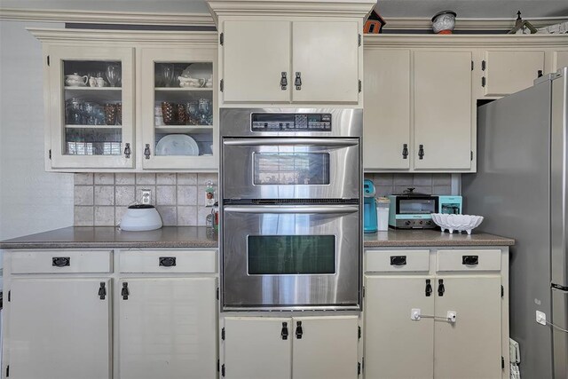 kitchen featuring glass insert cabinets, white cabinetry, appliances with stainless steel finishes, and decorative backsplash