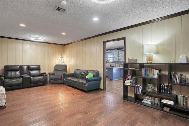 living area featuring crown molding, a textured ceiling, visible vents, and wood finished floors