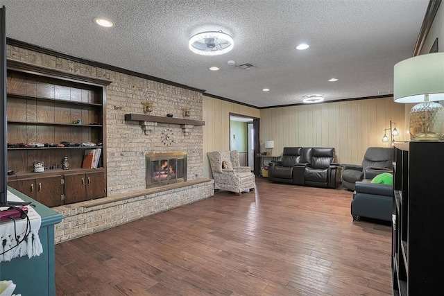 living room with a brick fireplace, ornamental molding, a textured ceiling, and wood finished floors