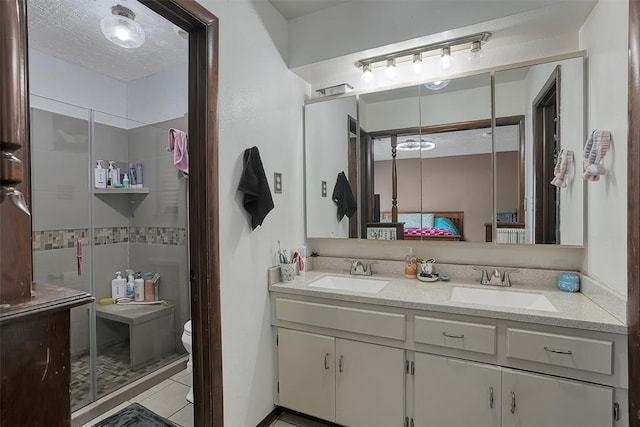 ensuite bathroom featuring a textured ceiling, double vanity, a stall shower, and a sink