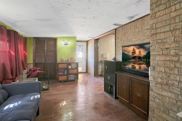 living area featuring visible vents, brick wall, and wood finished floors