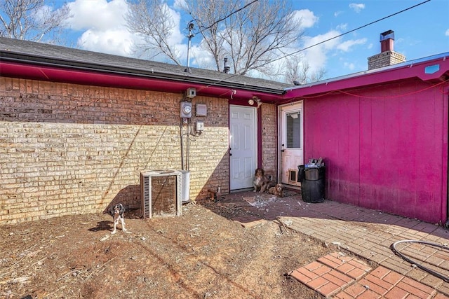 view of exterior entry featuring brick siding, a chimney, and cooling unit