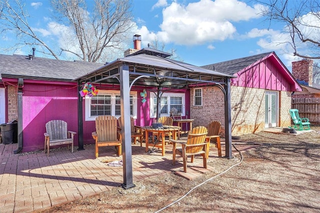 back of house featuring roof with shingles, a chimney, a gazebo, a patio area, and fence