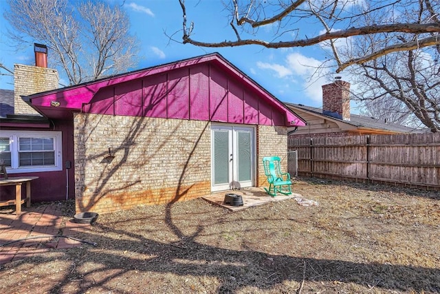 rear view of house featuring brick siding, fence, and a chimney