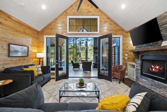 living room featuring wood finished floors, french doors, wooden walls, and a stone fireplace