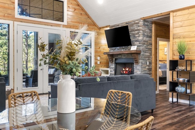 living area featuring lofted ceiling, wood walls, wood finished floors, and a stone fireplace