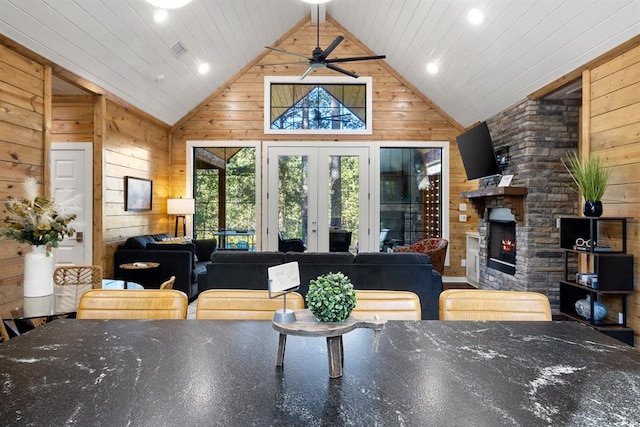 interior space featuring french doors, a fireplace, lofted ceiling, a ceiling fan, and wood walls