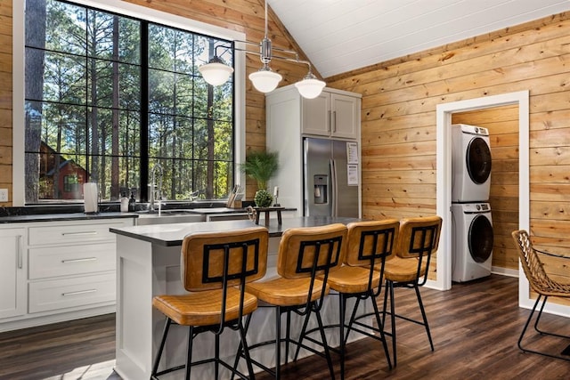 kitchen with vaulted ceiling, stainless steel fridge, stacked washer and clothes dryer, and wooden walls