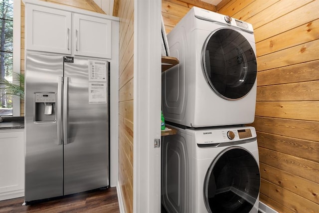 clothes washing area with wood walls, laundry area, dark wood-style flooring, and stacked washer and clothes dryer