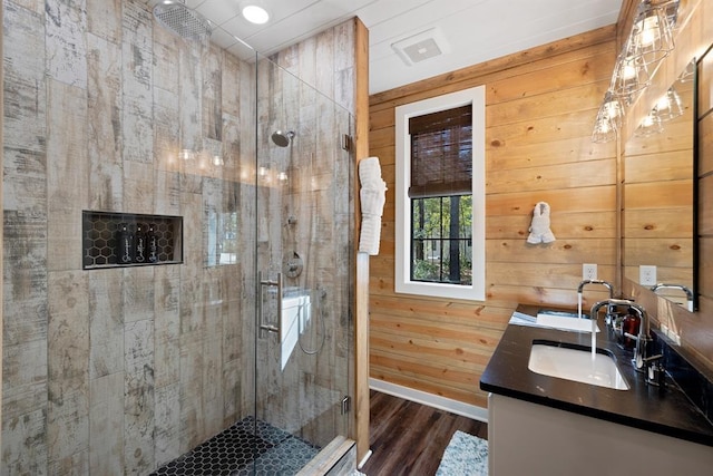 full bath with wooden walls, wood finished floors, vanity, baseboards, and a stall shower