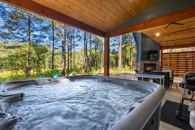 sunroom / solarium with a hot tub, a large fireplace, wood ceiling, and vaulted ceiling