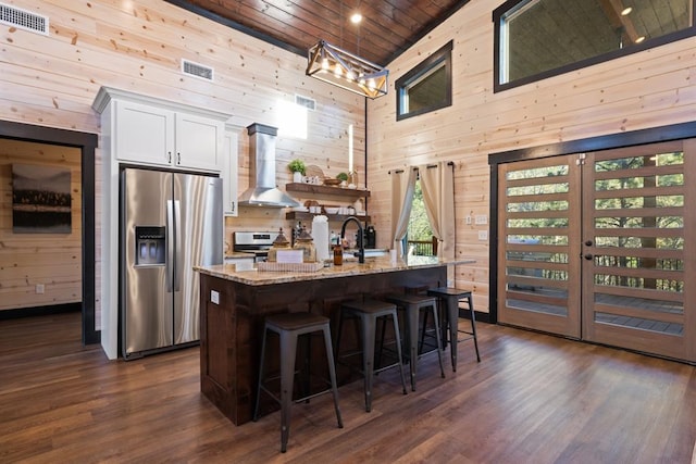 kitchen with wooden walls, wall chimney exhaust hood, visible vents, and appliances with stainless steel finishes