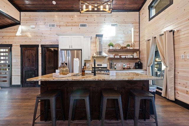 kitchen with wood walls, appliances with stainless steel finishes, white cabinetry, and wall chimney range hood