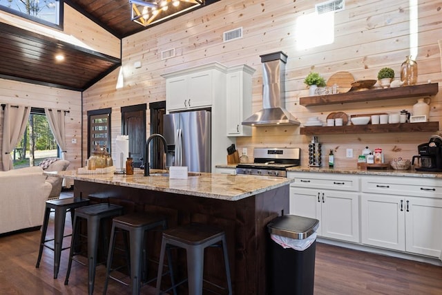 kitchen with visible vents, wall chimney range hood, wood walls, wood ceiling, and appliances with stainless steel finishes