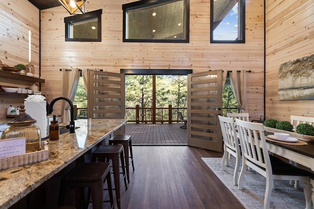 dining space featuring wood walls, a high ceiling, and dark wood-style flooring