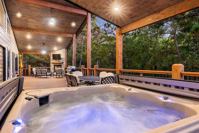 view of patio featuring an outdoor hot tub, an outdoor stone fireplace, a deck, and a ceiling fan