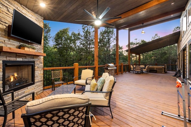 deck at dusk with ceiling fan and an outdoor living space with a fireplace