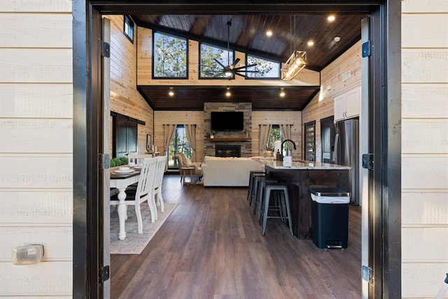 kitchen featuring open floor plan, a breakfast bar area, an outdoor stone fireplace, stainless steel refrigerator with ice dispenser, and dark wood-style flooring