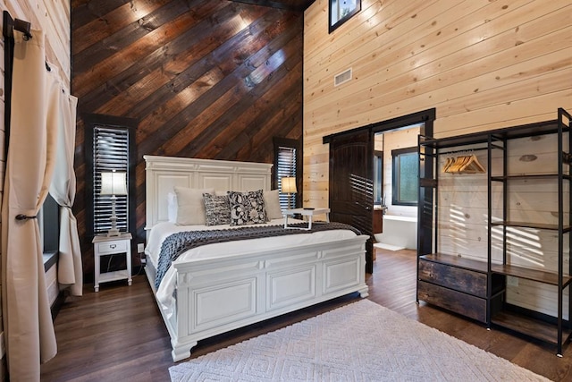 bedroom featuring visible vents, a barn door, wood walls, and dark wood-style flooring