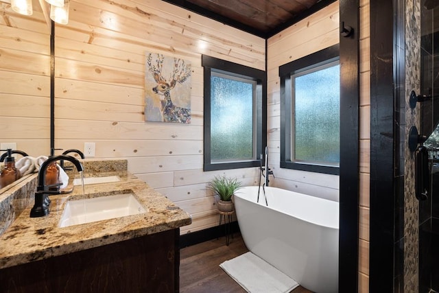 full bath featuring double vanity, wooden walls, a freestanding bath, and a sink