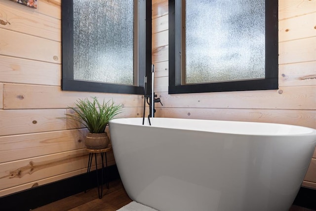 bathroom with a soaking tub, wood walls, and wood finished floors