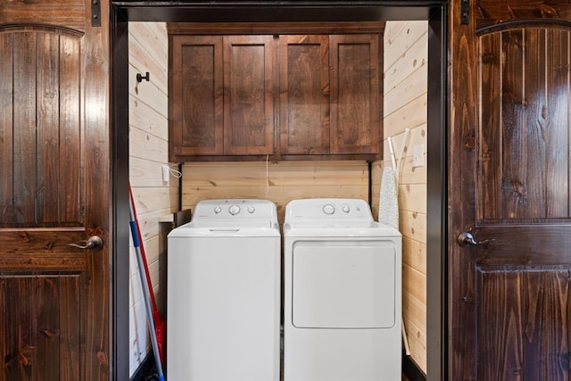 clothes washing area with washing machine and clothes dryer, wooden walls, and cabinet space