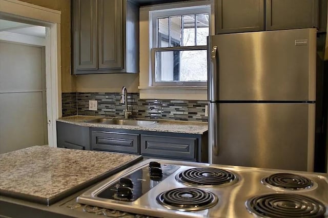 kitchen featuring tasteful backsplash, gray cabinets, stove, freestanding refrigerator, and a sink