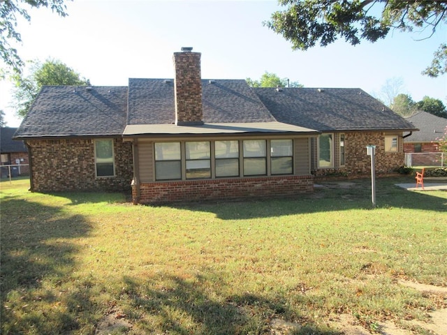 back of house featuring brick siding, a yard, a chimney, and roof with shingles