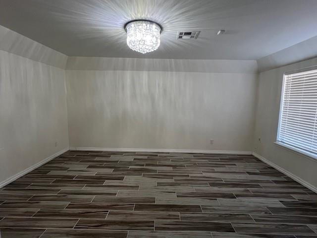 spare room with baseboards, wood finish floors, visible vents, and an inviting chandelier