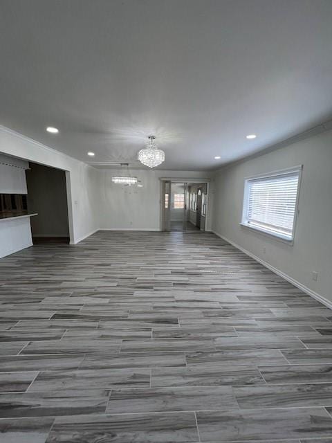 unfurnished living room with a chandelier, recessed lighting, a wealth of natural light, and crown molding